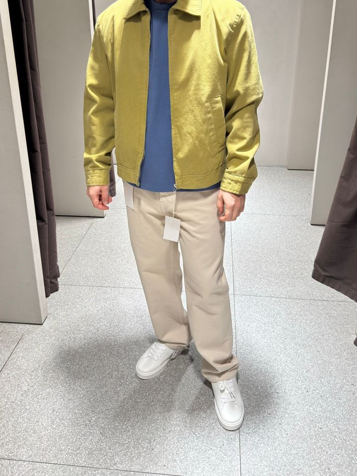 Olive zip jacket over a blue t-shirt with cream trousers